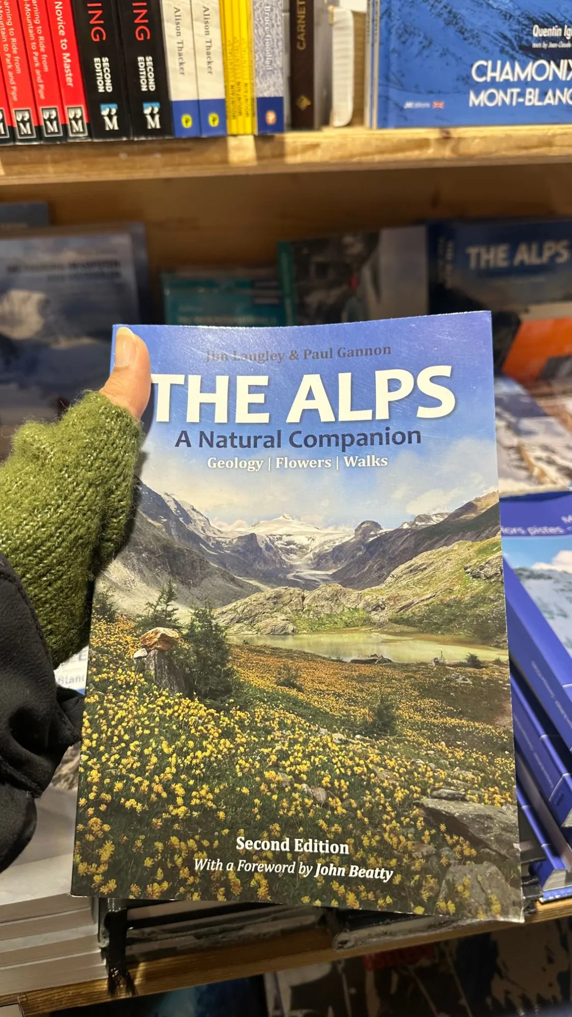 Holding 'The Alps: A Natural Companion' in a mountain bookshop