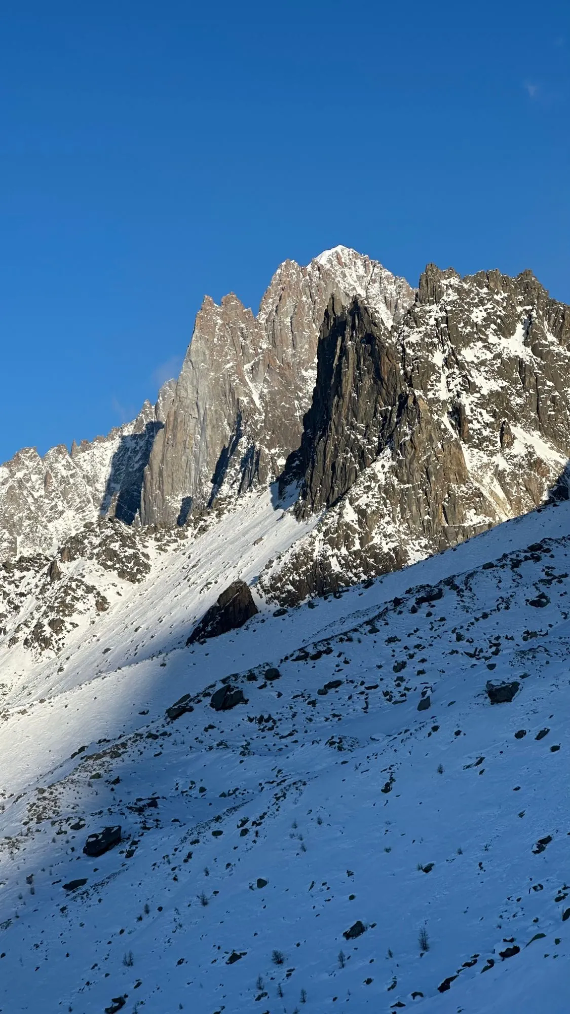 A jagged granite peak above a snowy slope under a deep blue sky