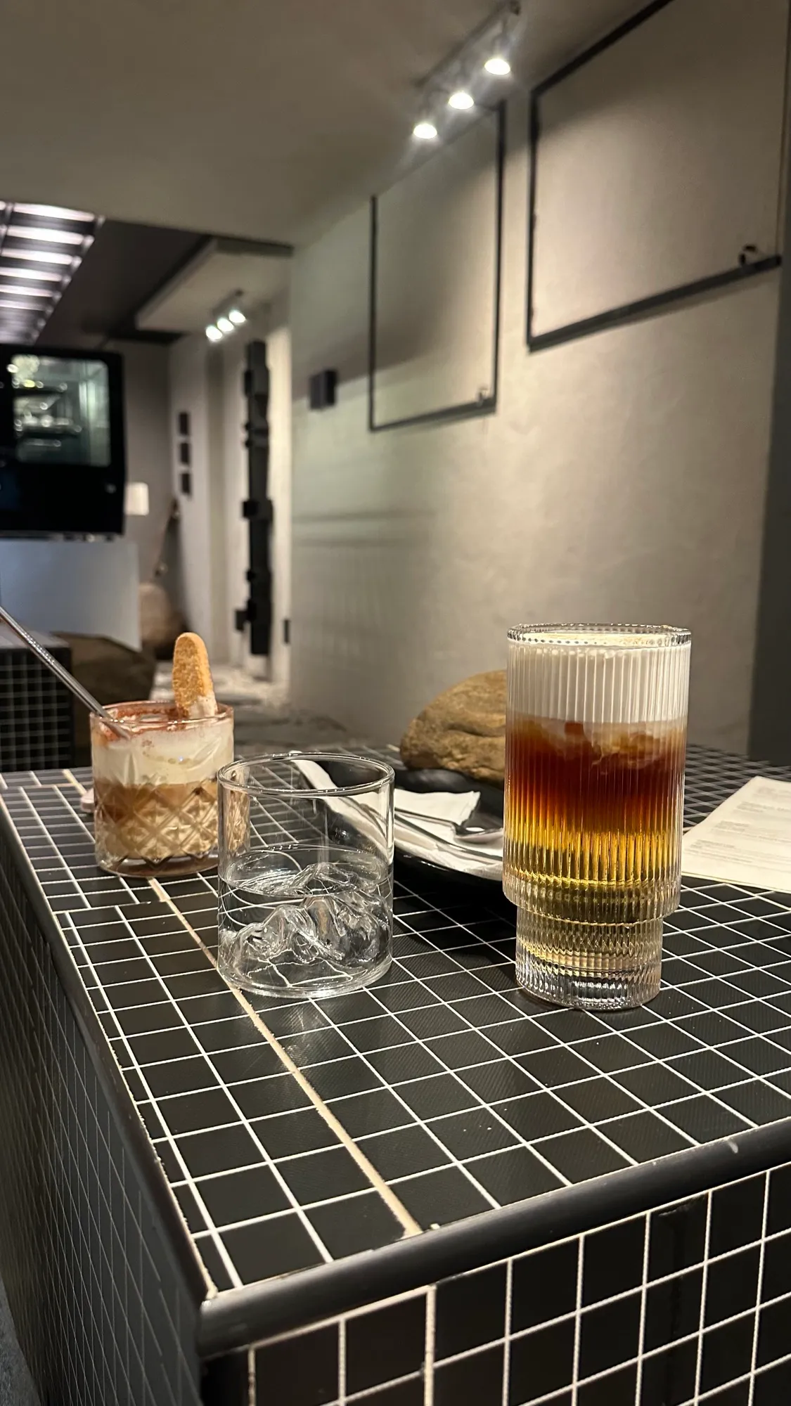 A layered iced coffee and a tiramisu on a black-tiled cafe counter