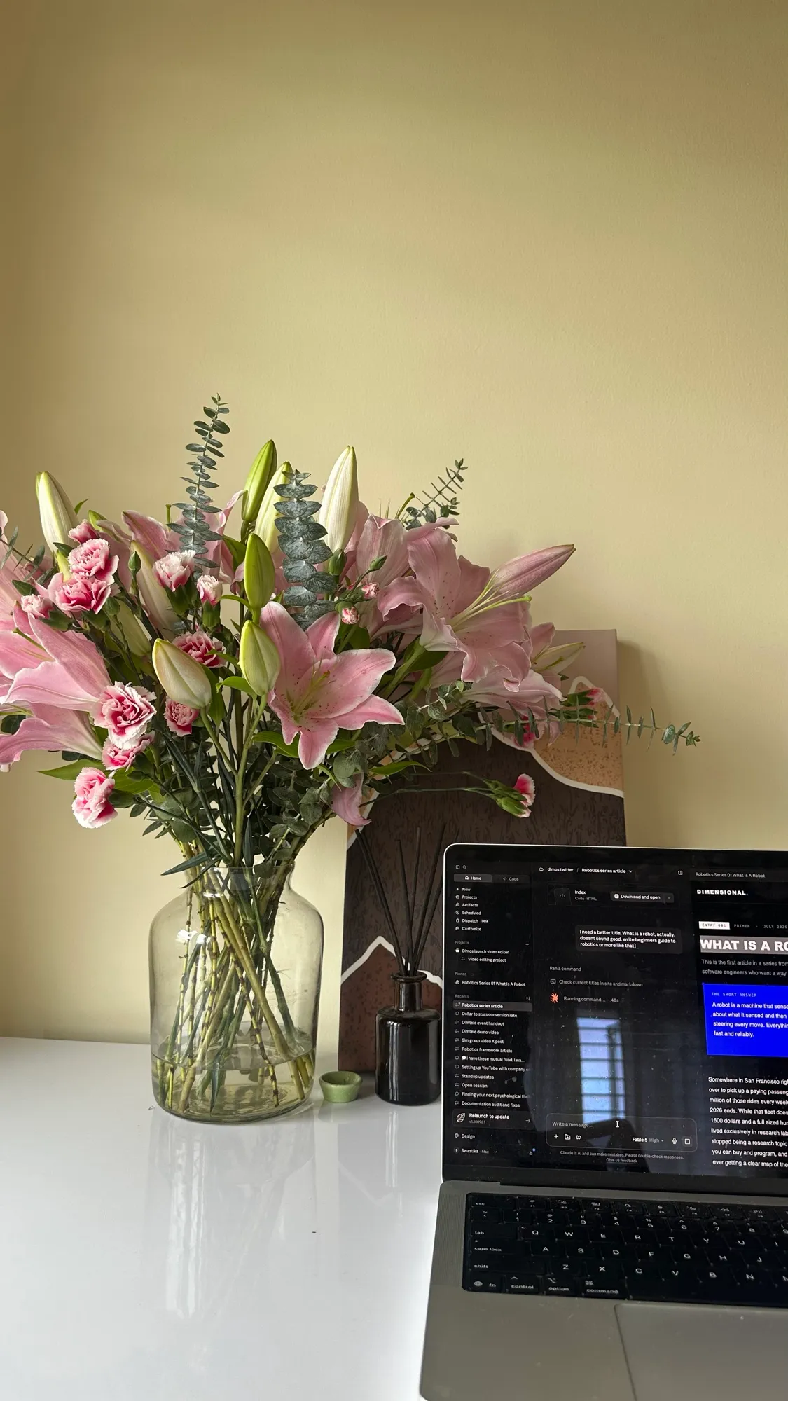 A vase of pink lilies and eucalyptus on the desk next to an open laptop