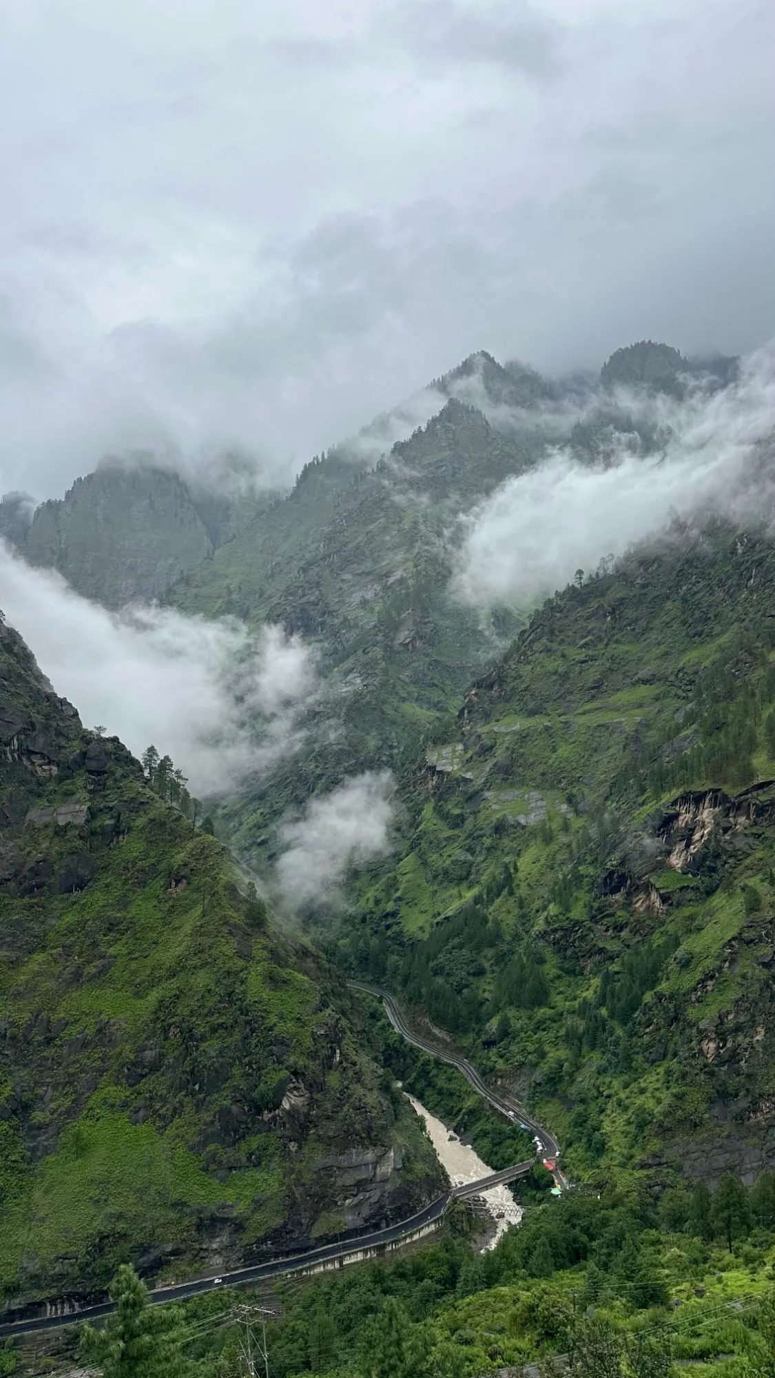 Clouds drifting through a deep green Himalayan valley with a road and river below