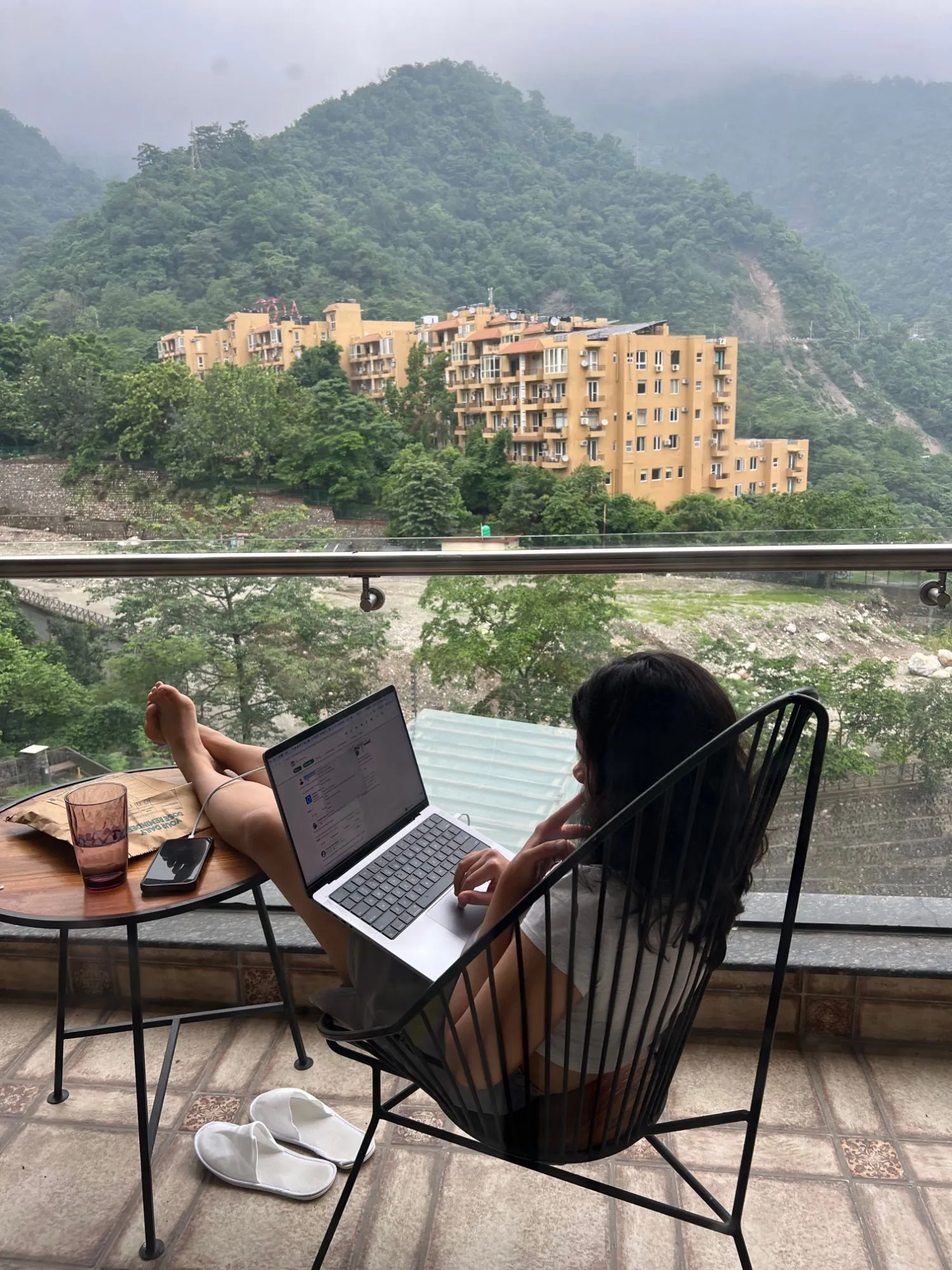 Working on a laptop from a balcony facing misty green mountains